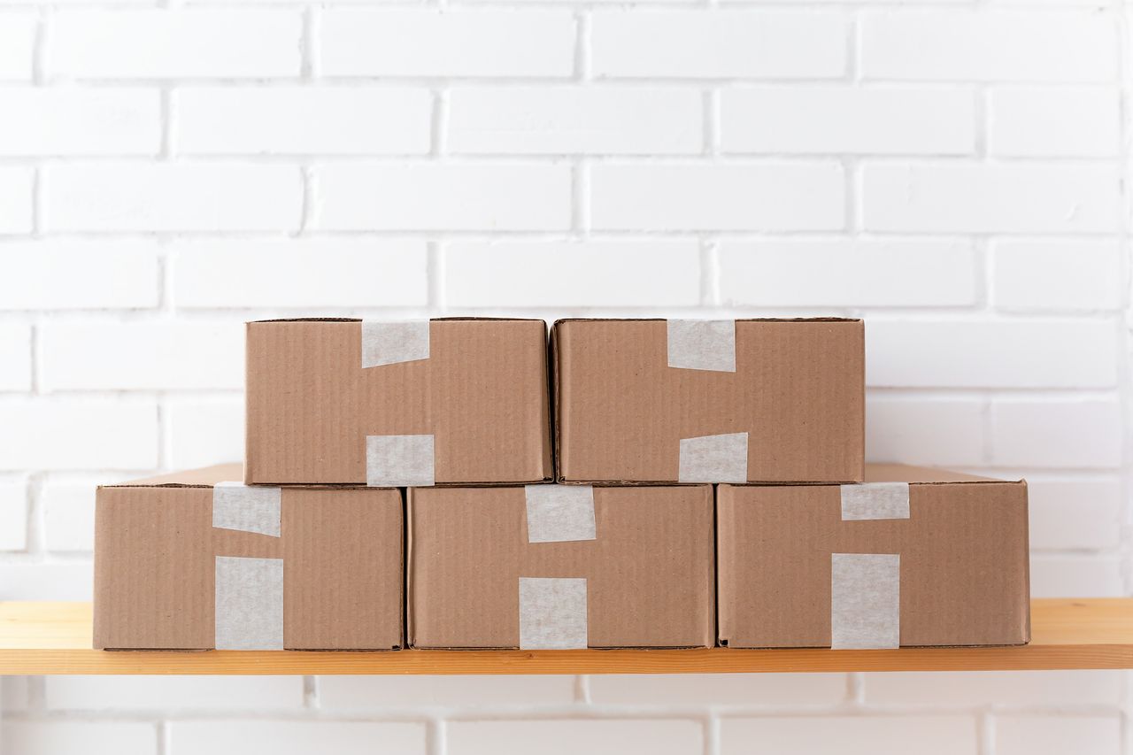 services-03 A neat stack of cardboard boxes taped and placed on a wooden shelf against a white brick wall.