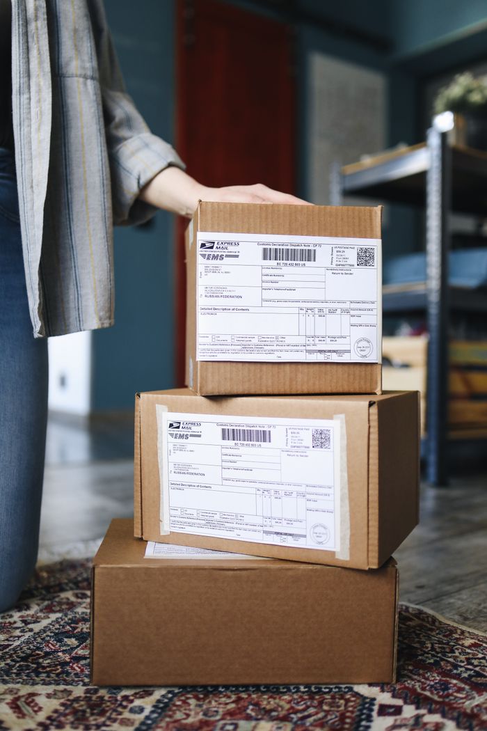 hero-img-01 A stack of brown cardboard boxes with shipping labels ready for mail delivery.